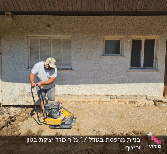 אדם עובד עם מכונה על קרקע חפורה ליד בית